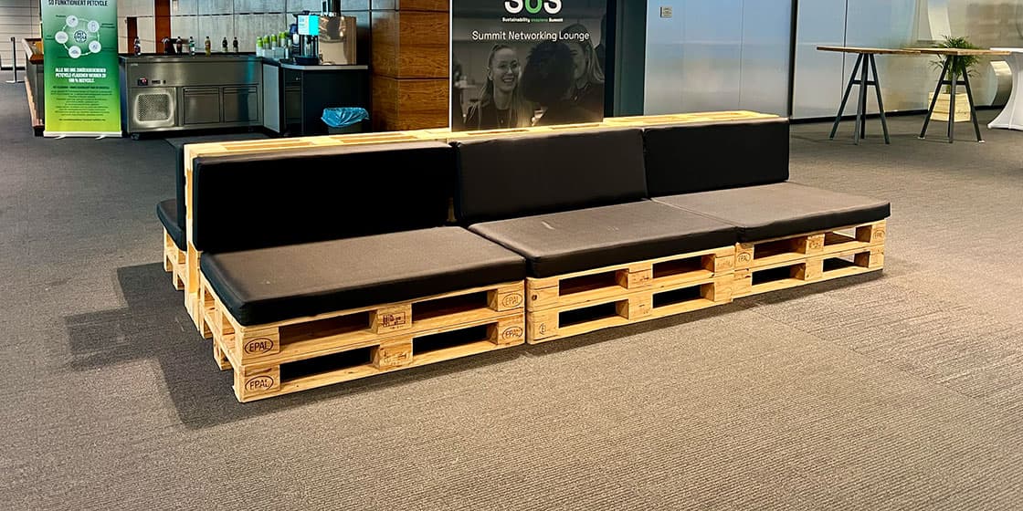 Networking-Lounge aus Palettenmöbeln auf einem Sustainability Summit – Sitzbänke mit schwarzen Sitzkissen und Rückenlehnen für Firmen-Event