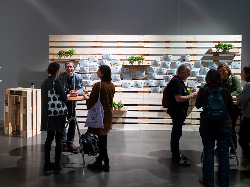 Palettenwand mieten Hamburg – Networking-Event vor modularer Palettenwand mit Visitenkarten und Notizen, Stehtisch im Vordergrund, Gäste im Gespräch