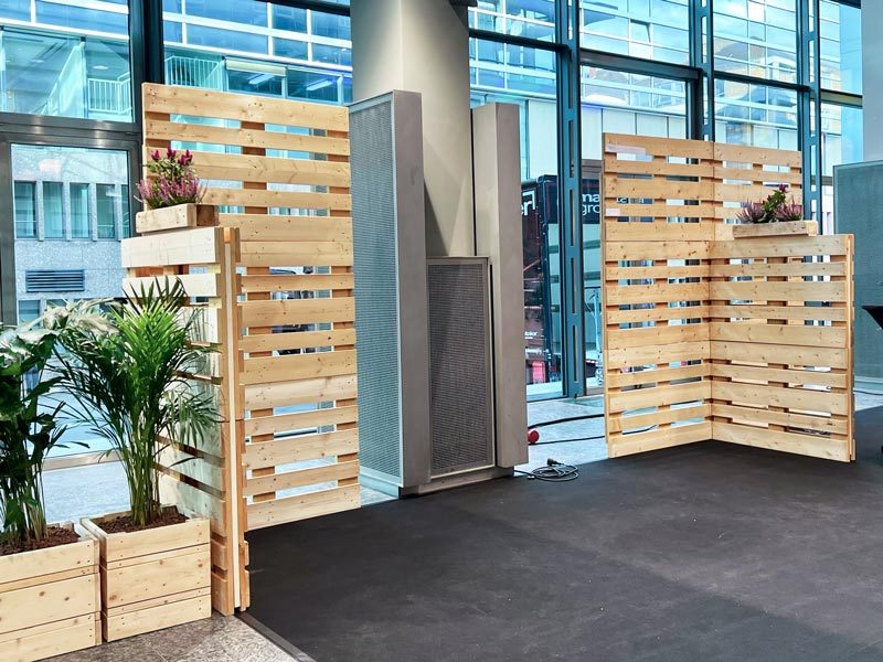 Palettenwand mieten Hannover – Zwei freistehende Palettenwände als Raumteiler in moderner Bürolobby mit Glasfront, dekoriert mit Pflanzgefäßen und Heidekraut