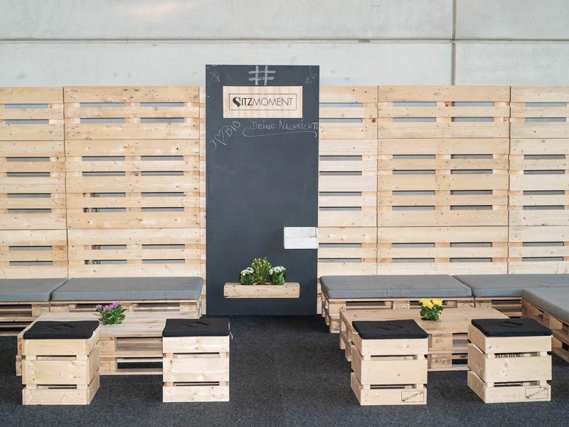 Tafelwand mieten Leipzig – Sitzmoment-Lounge mit zentraler Kreidetafel-Wand, beschriftet mit '#hybrid Deine Nachricht', umgeben von Palettenliegen und Hocker-Cubes